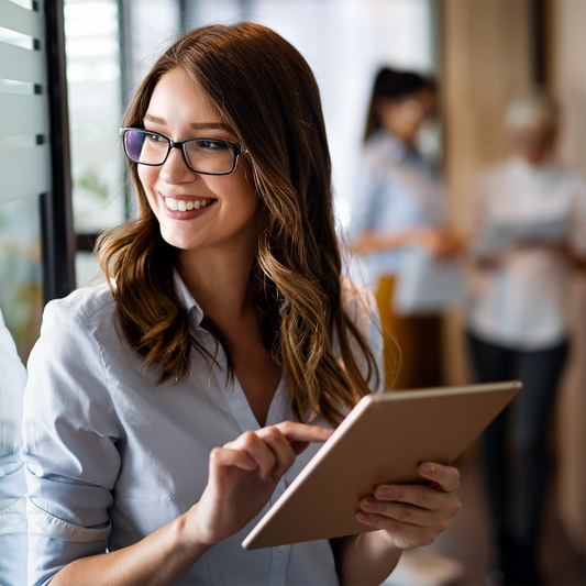 Young woman using a tablet in an office setting with blurred colleagues in the background
